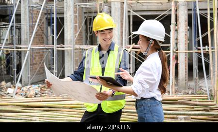 Two talented young Asian male and female civil engineer discussing and working together at the construction site. Stock Photo
