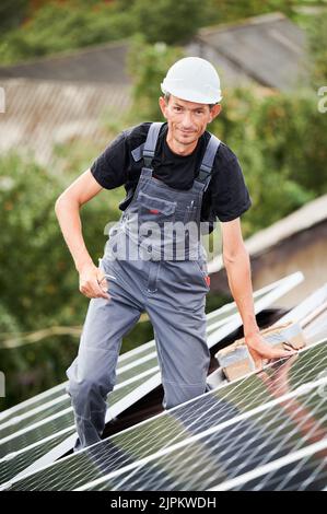 Portrait of man installer mounting photovoltaic solar moduls on roof of house. Electrician in helmet installing solar panel system outdoors. Concept of alternative and renewable energy. Stock Photo