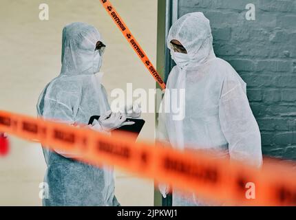 Forensic investigators collecting evidence at a murder scene in a building with barrier tape. Criminal researchers investigating a crime site and Stock Photo