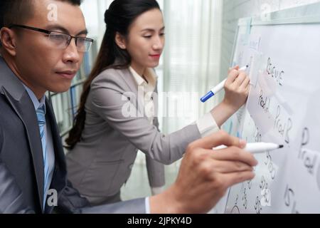 Vietnamese business people writing revenue plans on whiteboard Stock Photo