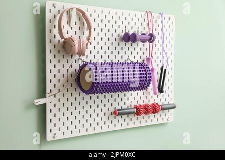 Pegboard with sports equipment and headphones on green wall Stock Photo
