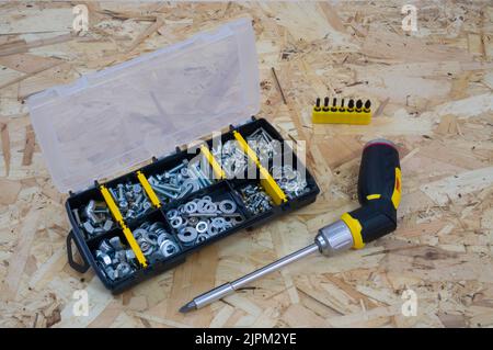 Case organizer with fasteners, a screwdriver and a holder with bits on a osb construction plate background. Stock Photo