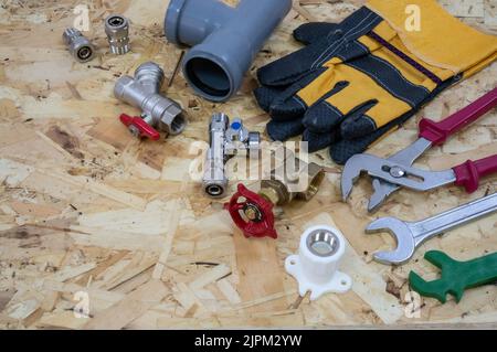 Plumbing tools, parts, pipeline components and gloves on the background of a construction OSB plate. Place for text or logo in left corner. Stock Photo
