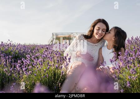 child kissing pregnant mother sitting in meadow near blooming lavender Stock Photo