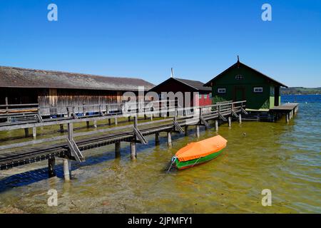 a long wooden pier leading to the colorful boat houses on lake Ammersee with sailing boats and the Alps in the background in the Bavarian Schondorf Stock Photo