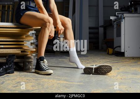 Female legs in carpenter shop, change of footwear Stock Photo