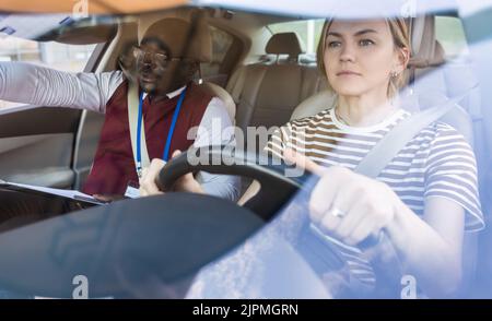 Driving school concept. A car instructor teaches a young woman how to drive. Teaching the rules of the road and driving a vehicle Stock Photo
