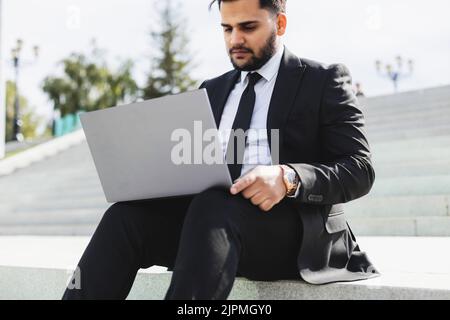 A man in a suit sits on the steps of a city staircase with a laptop. Working break. outdoors. business lifestyle Stock Photo
