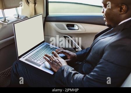 Business concept of a handsome dark-skinned man in a suit and glasses in the back seat of a luxury car working with a laptop. Copyspace and mockup Stock Photo