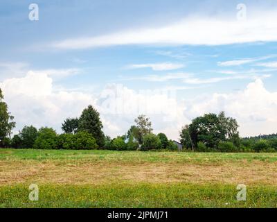 gray and white clouds in blue sky over mowed field after summer rain Stock Photo