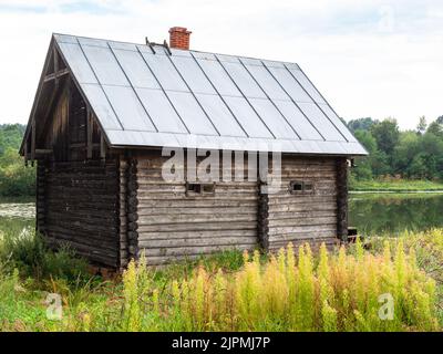 old log cabin on overgrown riverbank on summer day Stock Photo