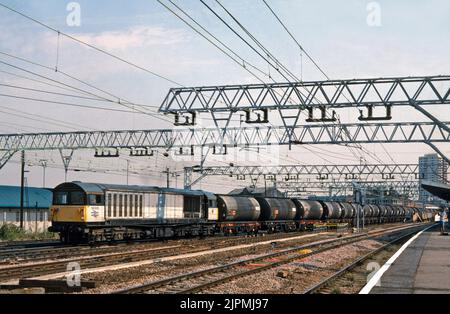 A Class 58 diesel locomotive number 58005 passes Stratford railway station in East London with a lengthy train of four wheel oil tanks on the 21st July 1994. Stock Photo