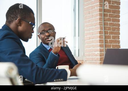 Two dark-skinned partners of an African American businessman in a meeting work on a laptop in the office. Affordable private courses and distance Stock Photo