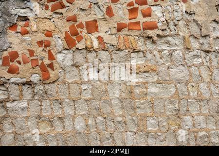 A section of pale stone built wall with randomly filed in areas in broken red tiles and mortar Stock Photo