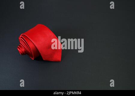 red color polyester fabric necktie rolled on black background with high angle Stock Photo