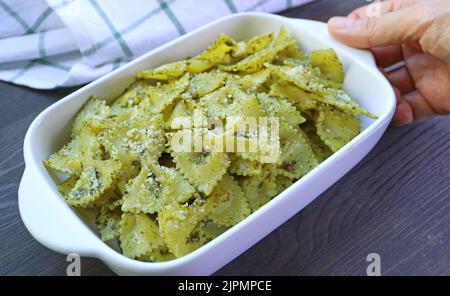Hand Placing a Bowl of Delectable Homemade Farfalle Pasta with Pesto Sauce on Wooden Table Stock Photo