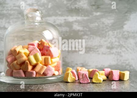 Pink and yellow heart shaped marshmallow in glass bell on gray concrete background. Romantic dessert in retro vintage pastel style. Mockup, template w Stock Photo
