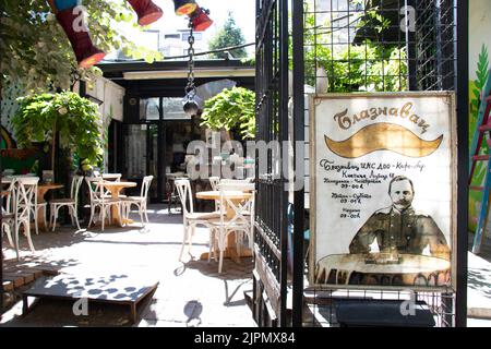 Belgrade-Serbia - June 15, 2022: Entrance to the garden of cafe-bar Blaznavac with outdoor sign board and chairs and tables inside a sunny garden Stock Photo