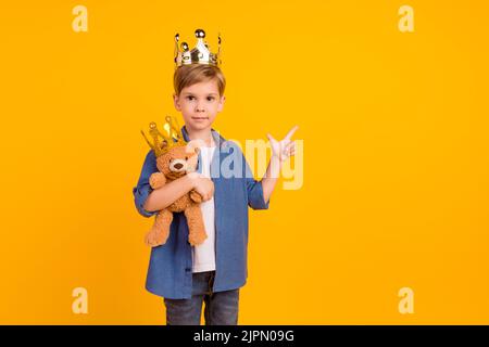 Portrait of positive person hold fluffy bear toy indicate finger empty space isolated on yellow color background Stock Photo