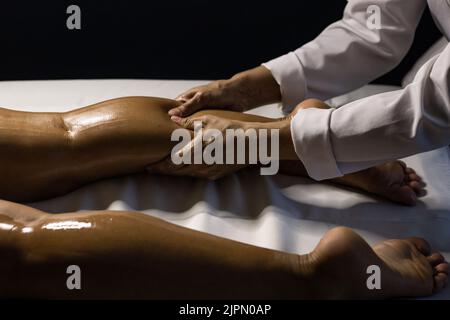 Goiânia, Goias, Brazil – July 18, 2022: A therapist dressed in white, massaging the leg of a patient lying on a stretcher, using therapeutic oil. Stock Photo