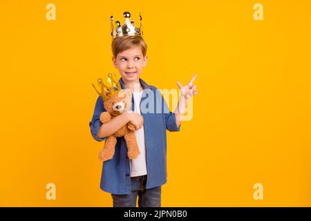 Photo of cheerful grandson look direct finger empty space hold soft bear toy isolated on yellow color background Stock Photo