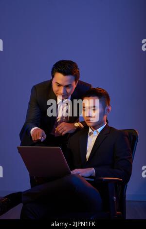 Young Vietnamese coworkers analyzing information on laptop screen Stock Photo