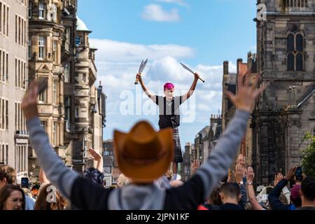 Edinburgh, Scotland, UK, 19th August 2022. Fringe performers on the Royal Mile: the street is packed with Fringe-goers, street performers on a sunny day. Pictured: a sword juggler. entertains the crowd Credit: Sally Anderson/Alamy Live News Stock Photo