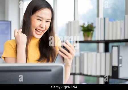 Portrait happy young programmer Asian woman work at start up technology office and using smartphone and testing mobile application and excited in succ Stock Photo