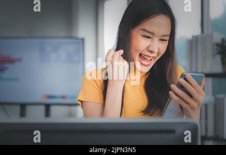 Portrait happy young programmer Asian woman work at start up technology office and using smartphone and testing mobile application and excited in succ Stock Photo