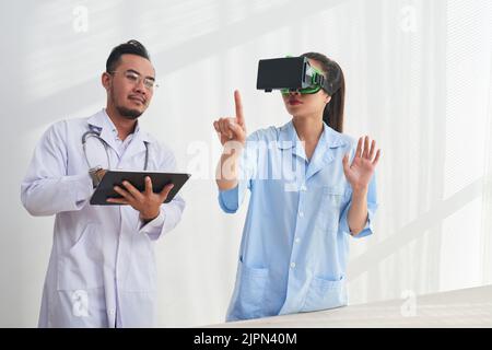 Talented team of doctors gathered together at modern laboratory and conducting experiment with help of digital tablet and VR headset Stock Photo