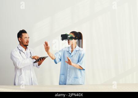 Unrecognizable young nurse wearing uniform using VR headset while carrying out experiment at modern laboratory with colleague, white background Stock Photo