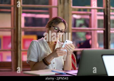 Female employee using mobile device at workplace, young woman freelancer distracted by smartphone Stock Photo