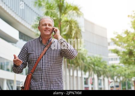 Cheerful mature man walking in the street and calling on smartphone Stock Photo