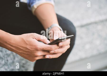 Close-up shot of male hands using modern smartphone, blurred background Stock Photo