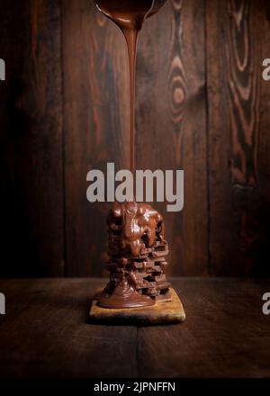 Pouring melted hot chocolate over a pile of chocolate bars on a rustic wooden table Stock Photo