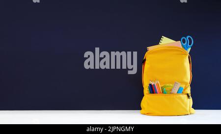 Backpack with different colorful stationery on table and blue background. Banner design back to school concept background. Blue chalkboard Stock Photo