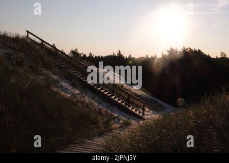 Wooden stairs to the beach covered with sand in surreal morning light. Low key abstract landscape. Lubiatowo sand dunes, foot path in nature park with Stock Photo
