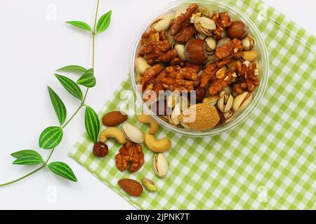 Pistachios, walnuts, cashew nuts, hazelnuts, peanuts, almonds in bowl on green and white checkered cloth Stock Photo