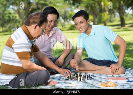 Vietnamese teenager playing chess with his father and grandfather in llcal park Stock Photo