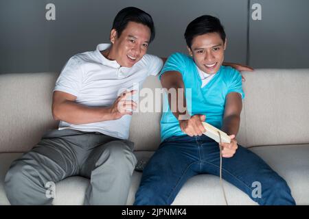 Father giving advice to his son who is playing video game Stock Photo