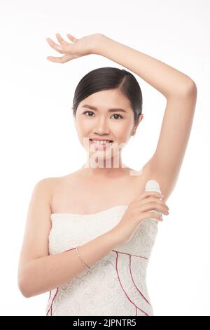 Smiling pretty young Asian woman applying deodorant Stock Photo