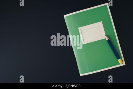 top down view of small green notebook and pencil stub on dark table Stock Photo
