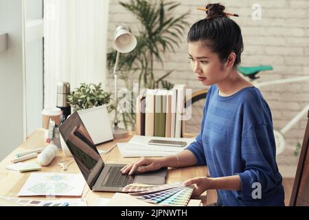 Young Vietnamese web designer with color palette working on laptop in her studio Stock Photo