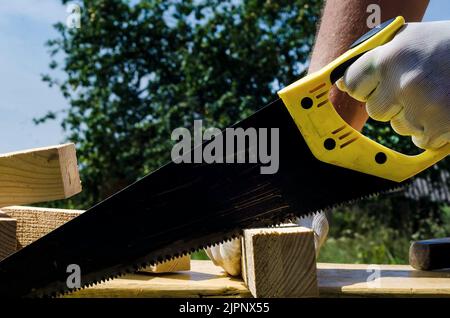 A hand with a hacksaw cuts a wooden board or beam. Construction Stock Photo