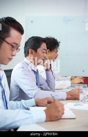 Asian entrepreneur reading document and calling to business partner Stock Photo