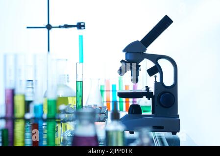 Laboratory interior: test tubes and flasks with colorful liquids, modern microscope standing on bench, no people Stock Photo