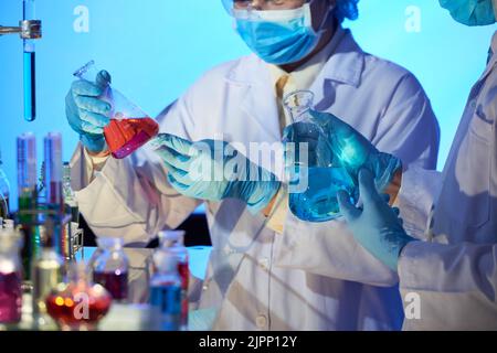 Group of chemists wearing safety goggles and white coats studying content of flasks while analyzing results of conducted experiment Stock Photo