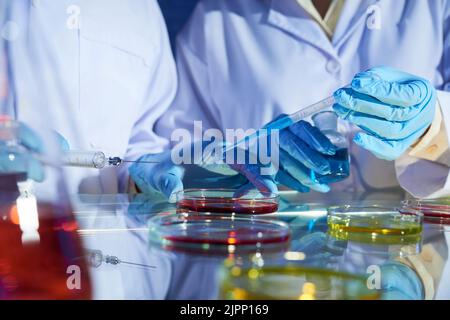 Close-up shot of unrecognizable researchers pouring blue liquid into Petri dish with other substance while working together on new project Stock Photo