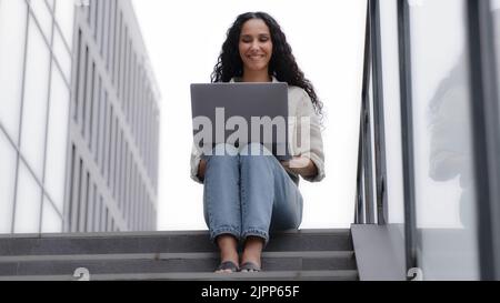 Busy concentrated woman user freelancer worker specialist professional female businesswoman sitting outdoors on stairs in downtown with laptop working Stock Photo