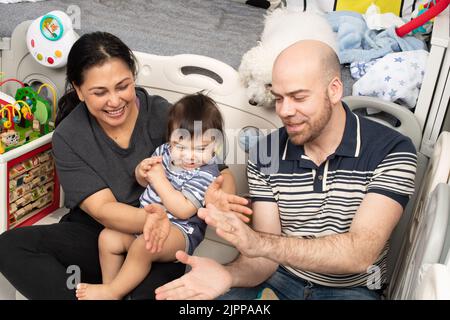 11 month old baby boy at home with parents singing song with hand gestures Stock Photo